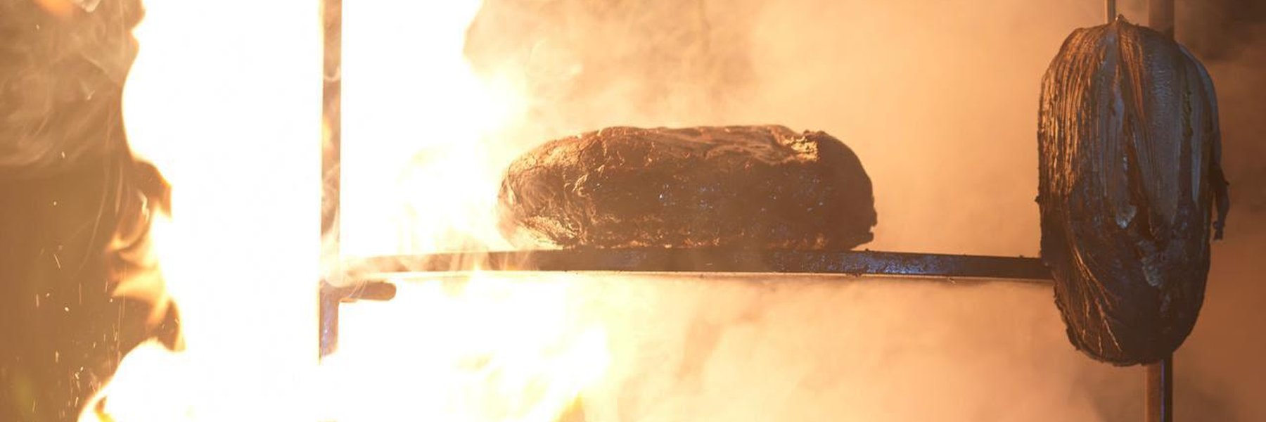 Cooking over an open fire: meat on a hanging rack in the smoke, a pot on the embers